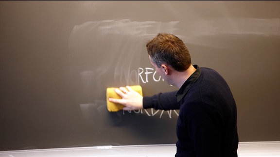 Lehrer wischt eine Tafel ab.