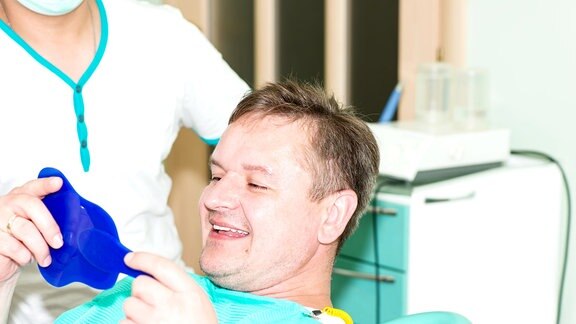Mann betrachtet beim Zahnarzt seine Zähne im Spiegel
